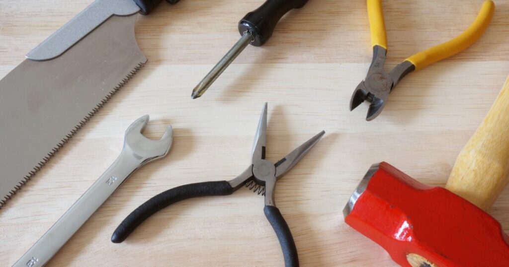木材の上に並べられたノコギリやドライバーなどの大工工具